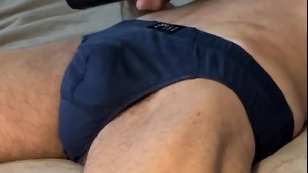 Retorciéndose y estirándose en la cama con ropa interior oscura y calzoncillos con 2 pistolas de masaje concentrándose en la zona pélvica y de la ingle.